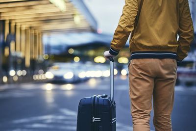 Rear view of mid adult man with luggage standing on street at airport