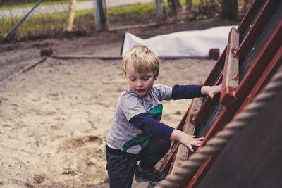 Side view of cute boy climbing on ladder outdoors