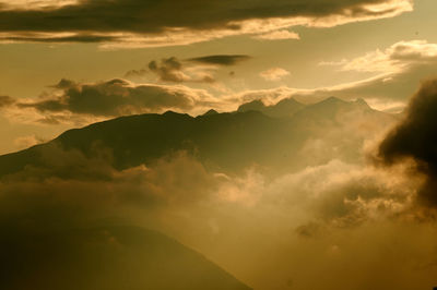 Low angle view of dramatic sky over silhouette mountains during sunset