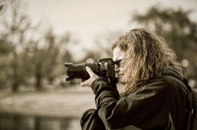 Woman photographing through camera against trees
