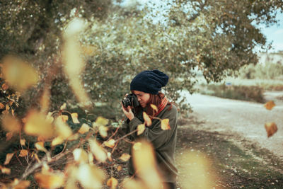 Woman photographing with camera while standing in forest