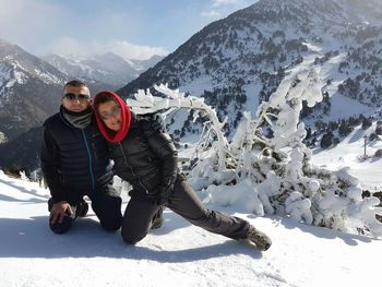 Portrait of couple kneeling on snowcapped mountains during winter