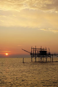 Silhouette cranes on sea against sky during sunset