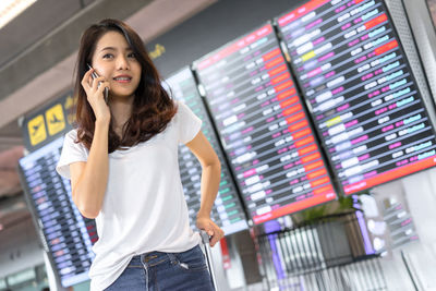 Young woman using phone while standing on laptop