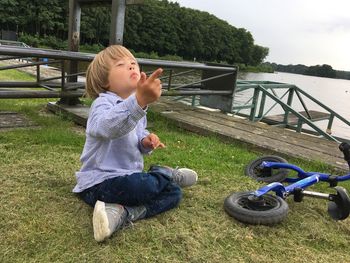 Boy playing on grass by lake against sky