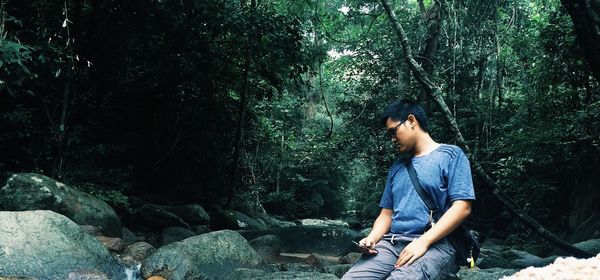 Young man sitting on rock in forest