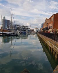 Sailboats moored on canal amidst buildings in city against sky