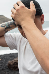 Close-up of man adjusting hat while standing against sky