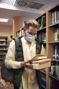 A young boy with a mask is reading several books in a library