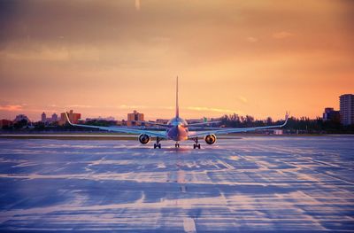 Airplane on airport runway against sky during sunset