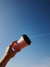 Low angle view of hand holding umbrella against clear blue sky