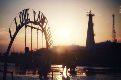 Silhouette people at amusement park against sky during sunset