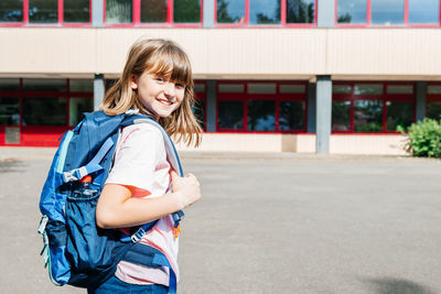 Portrait of a happy schoolgirl girl with a backpack on her back against the school.