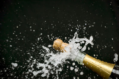 Close-up of champagne splashing from bottle over black background 