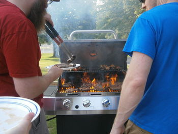 Side view of man serving sausages to friend by burning barbecue