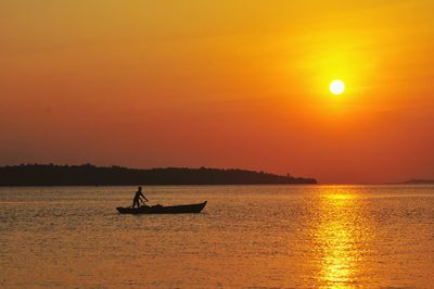 Silhouette fisherman boating on sea during sunset