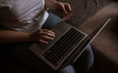 Young woman looking at the market on laptop with card on hand