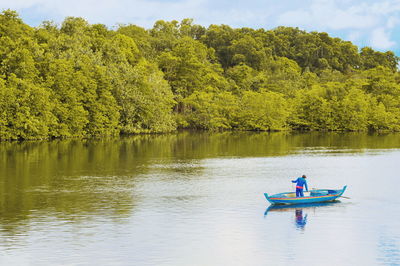 Fisherman fishing in lake while standing on boat against trees