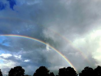 Low angle view of rainbow over trees against sky