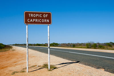 Sign by empty road against clear blue sky