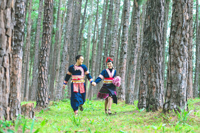 Couple hmongs holding hands and running in the pine wood, man and woman in hmong clothes