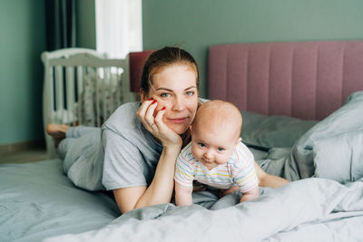 Portrait of a young caucasian beautiful mom and baby on the bed in the bedroom. domestic live