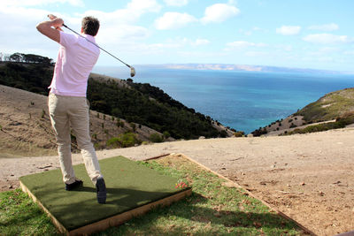 Rear view of man playing golf against sea