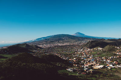 Aerial view of townscape by mountain against blue sky