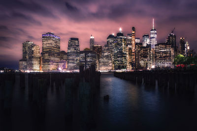 Illuminated buildings by river against sky at night