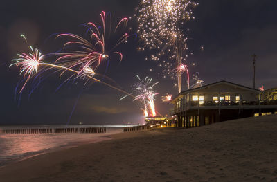 Firework display at beach against sky at night