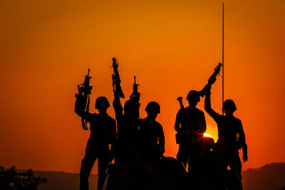 Silhouette army soldiers with weapons against sky during sunset