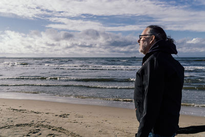 Portrait of young woman standing at beach against sky