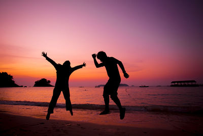 Silhouette friends standing at beach against sky during sunset