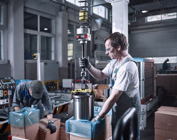 Worker using indoor crane for lifting metalsocket from cardboard box