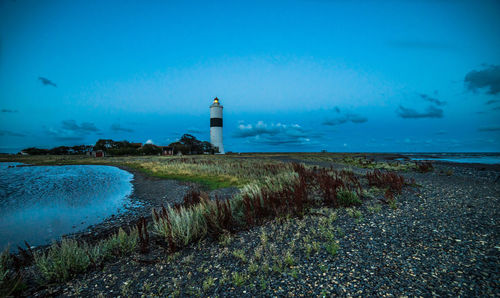 Lighthouse on calm sea against blue sky