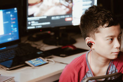 Boy wearing headphone looking away against computer