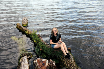 Rear view of woman sitting on rock by lake