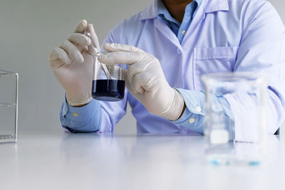 Midsection of scientist holding liquid on table in laboratory
