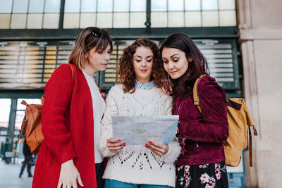 Cheerful women holding map while standing outdoors