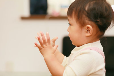 Side view of cute baby girl clapping hands while standing at home