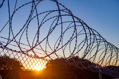 Barbed wire fence against sky during sunset