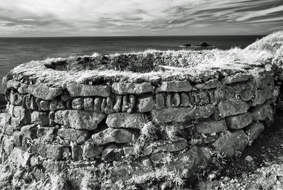 Stone wall by sea against sky