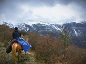 Rear view of man horseback riding against mountains