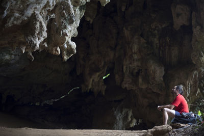 Rear view of woman sitting on rock in cave