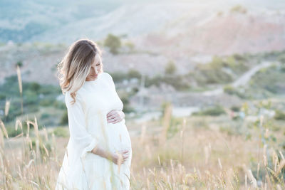 Pregnant woman holding belly standing on field