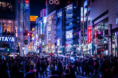 Crowd on street amidst illuminated buildings at night