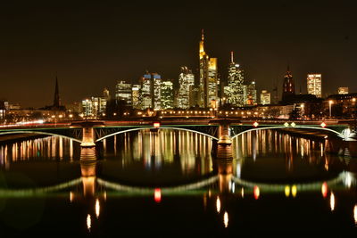 Illuminated buildings by river against sky at night