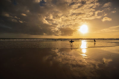 Silhouette people on beach against sky during sunset