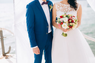 Midsection of woman holding bouquet against white wall