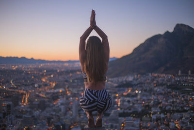 Rear view of woman standing by cityscape against sky during sunset